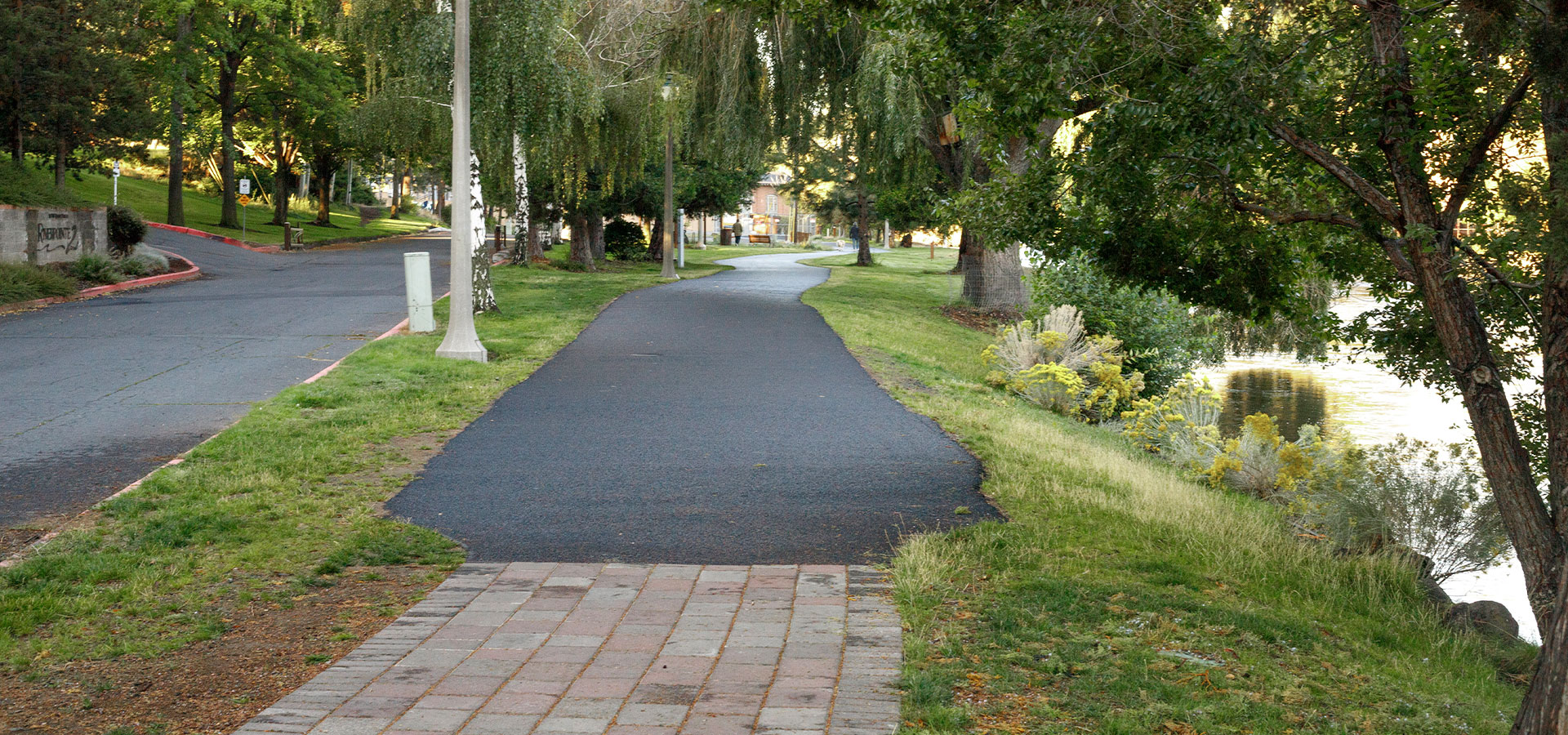 Paved and asphalt path along the grassy riverbank at Pacific Park
