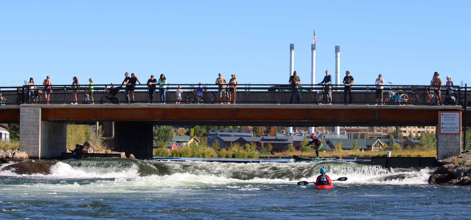 Onlookers on a pedestrian bridge watching the Bend Whitewater Park.