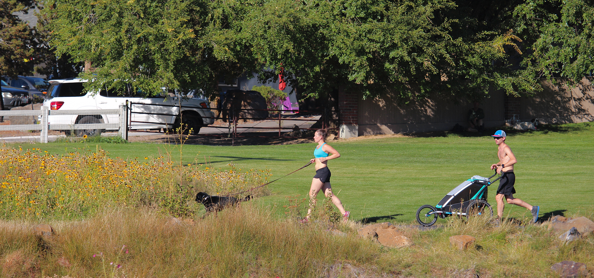 A woman and a dog and a man pushing a stroller and jogging on a path at Miller's Landing.