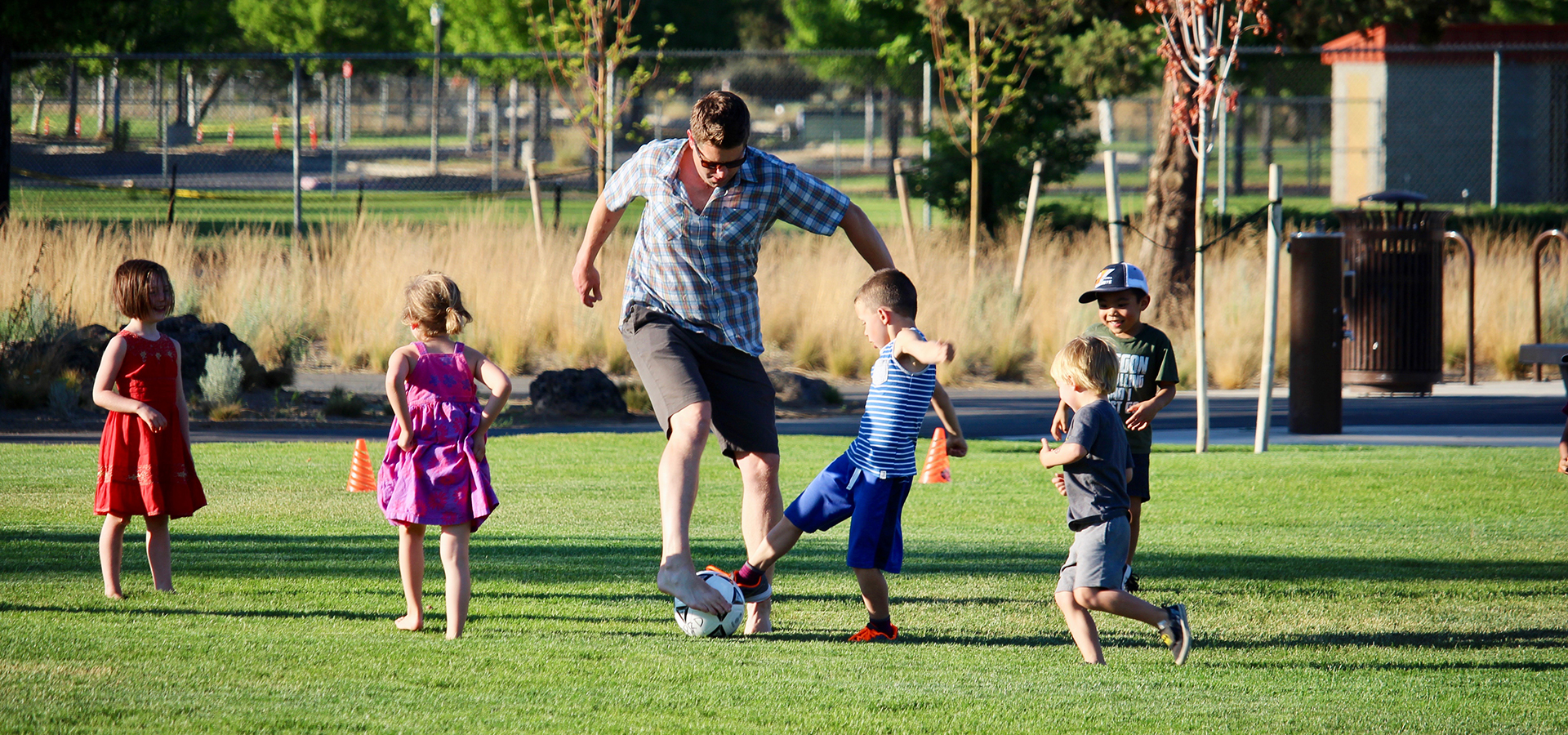 kids and an adult playing soccer in the grass