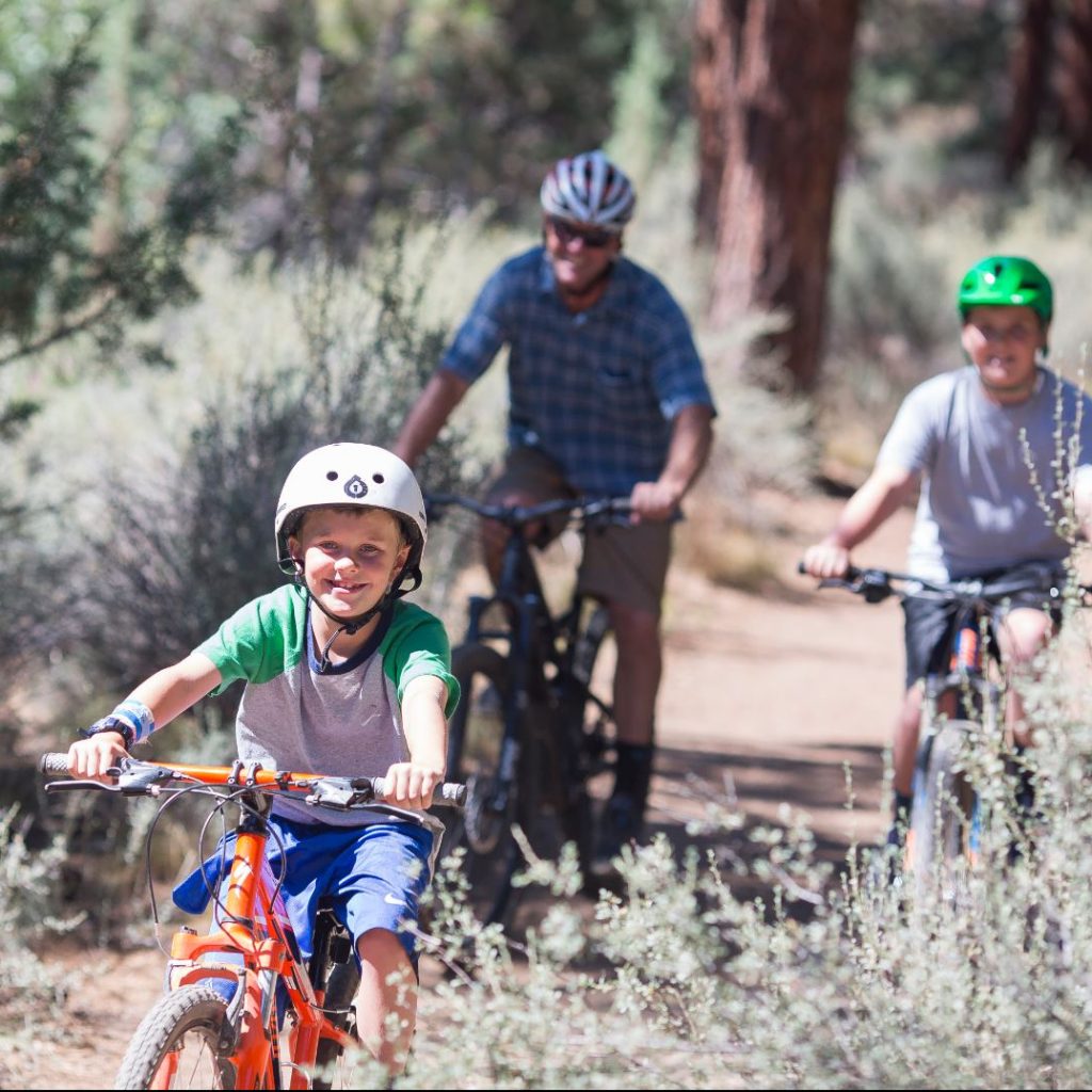 A smiling child on bike leads two other riders on trail through Shevlin Park