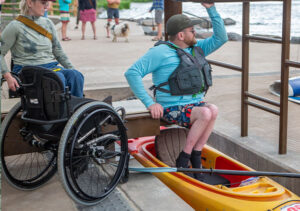 Patron moving from wheelchair to kayak at Miller's landing roller launch.