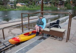Patron using the pull out bench of the roller ramp to get the correct height to transfer onto their kayak.