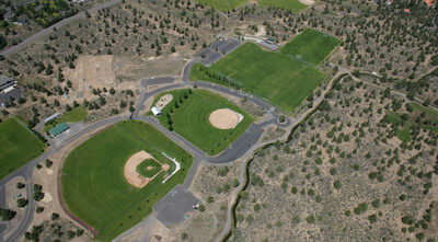 ariel view of Big Sky Park featuring three separate field areas including two baseball/softball fields and parking lots with natural land surrounding the park