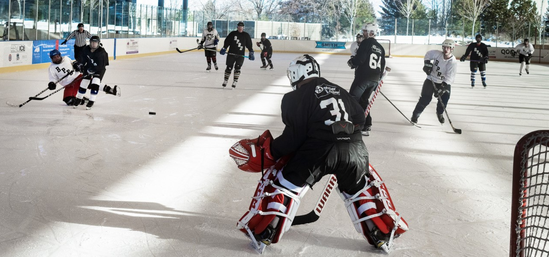 At the Pavilion, a hockey goalkeeper watches as teammate knocks down opposing player.