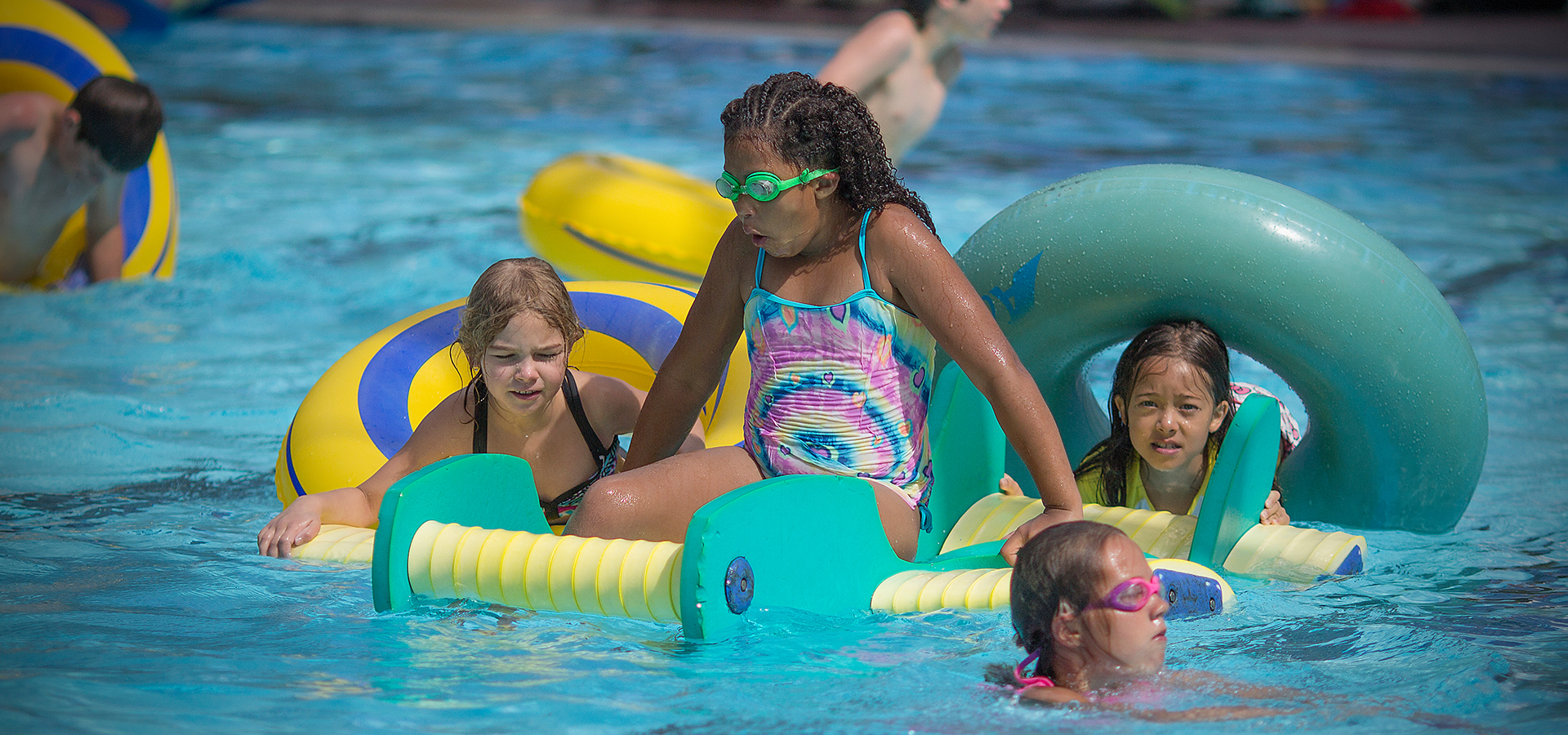 Kids playing on floaties in the pool.