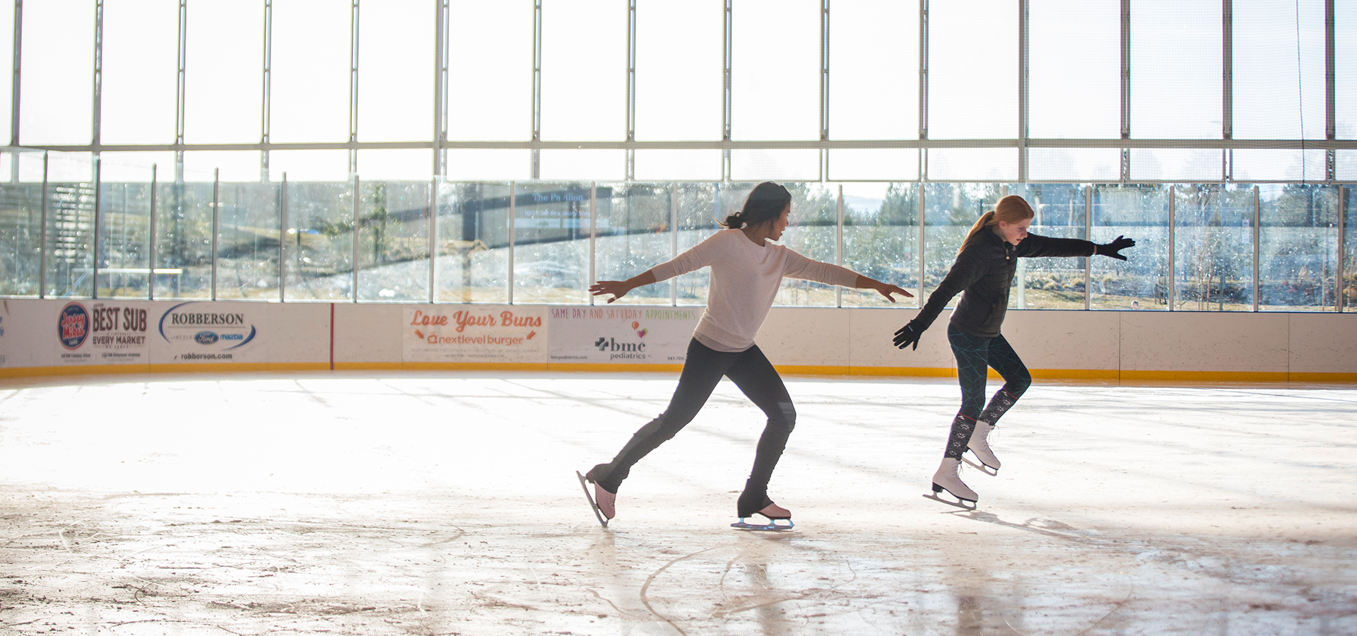 A woman showing a young girl an ice skating move.