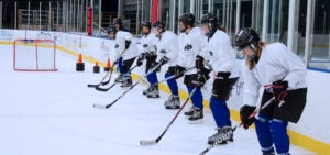 A group of women in hockey gear line up on the ice rink for practice