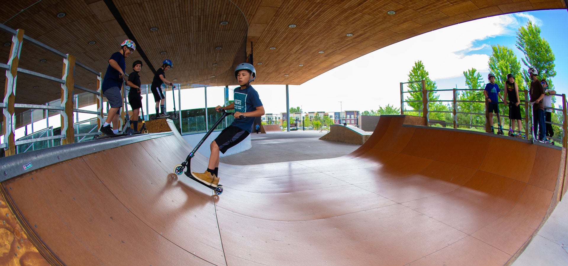 A boy on a scooter is riding the half-pipe ramp at the Pavilion.