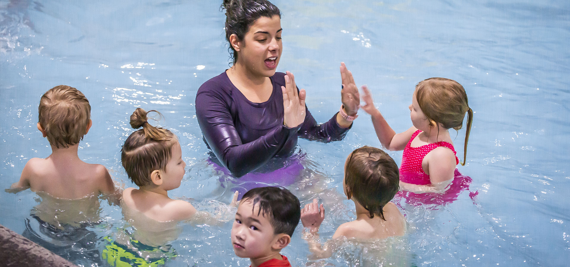 An instructor is addressing a group of five children in the pool at Juniper