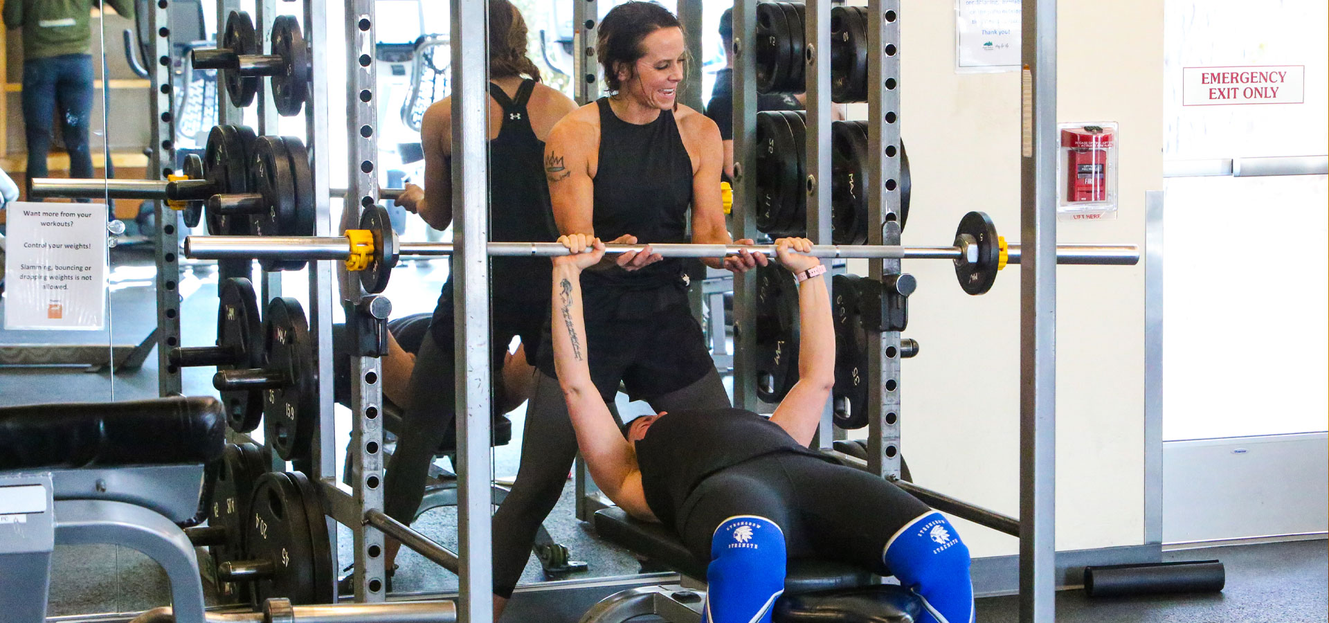 A woman is spotting another woman while bench pressing at Juniper fitness center