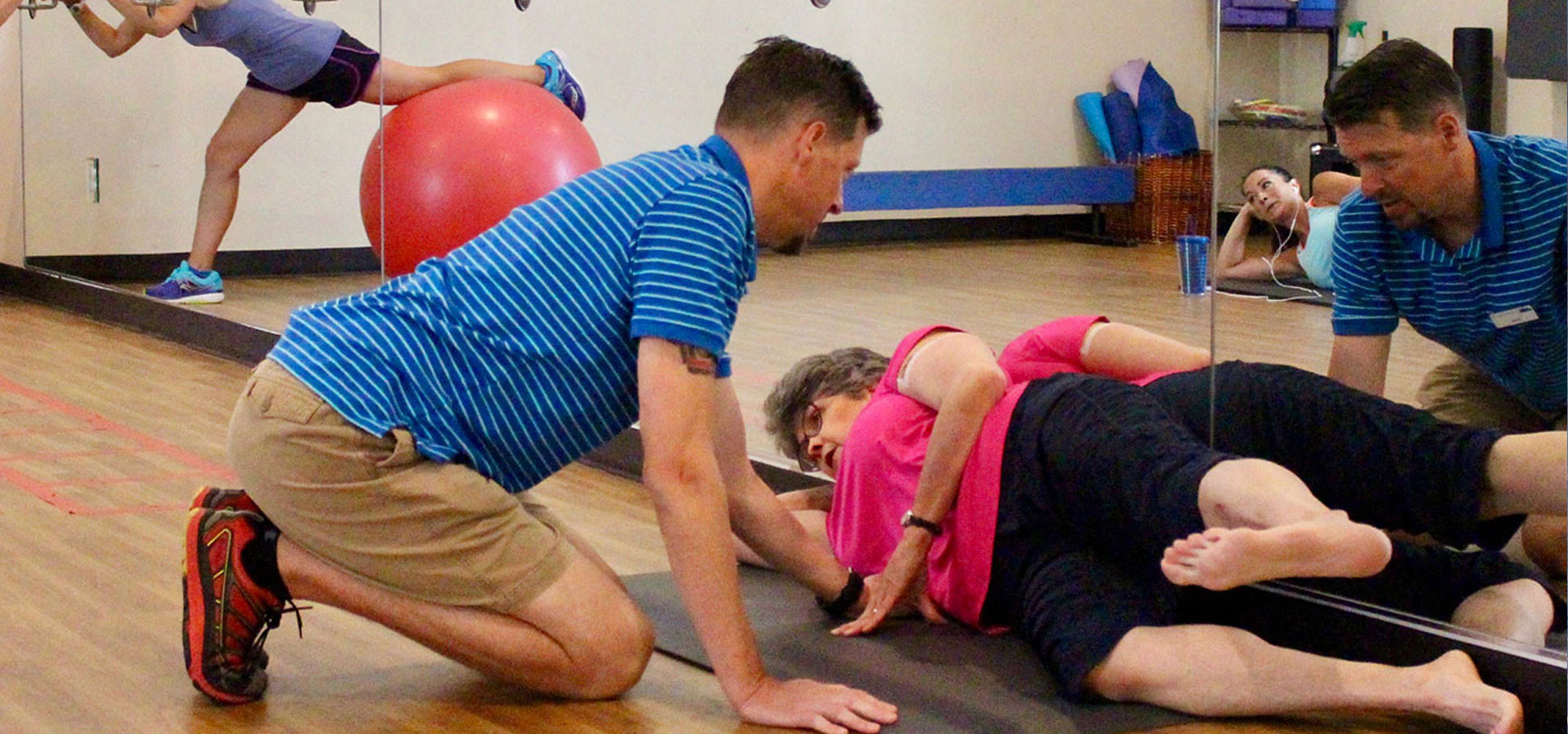 A personal trainer is helping a patron stretch in the fitness room.