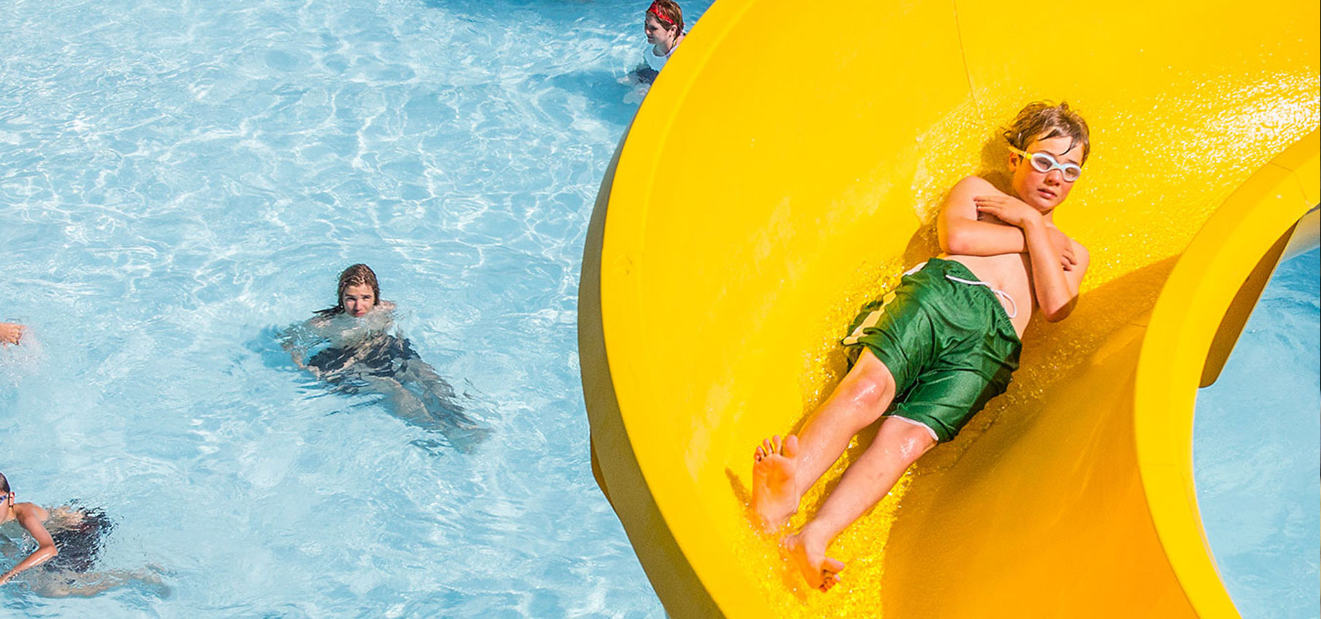 A kid is riding down the yellow water slide at Juniper.