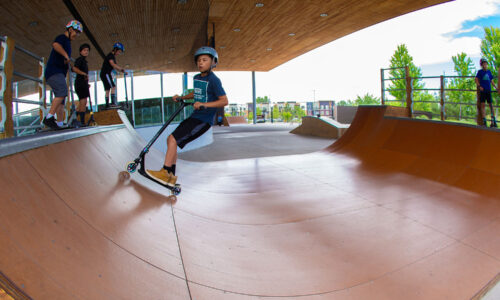 Group of kids with scooters and skateboards using the skate park feature at the PAC.