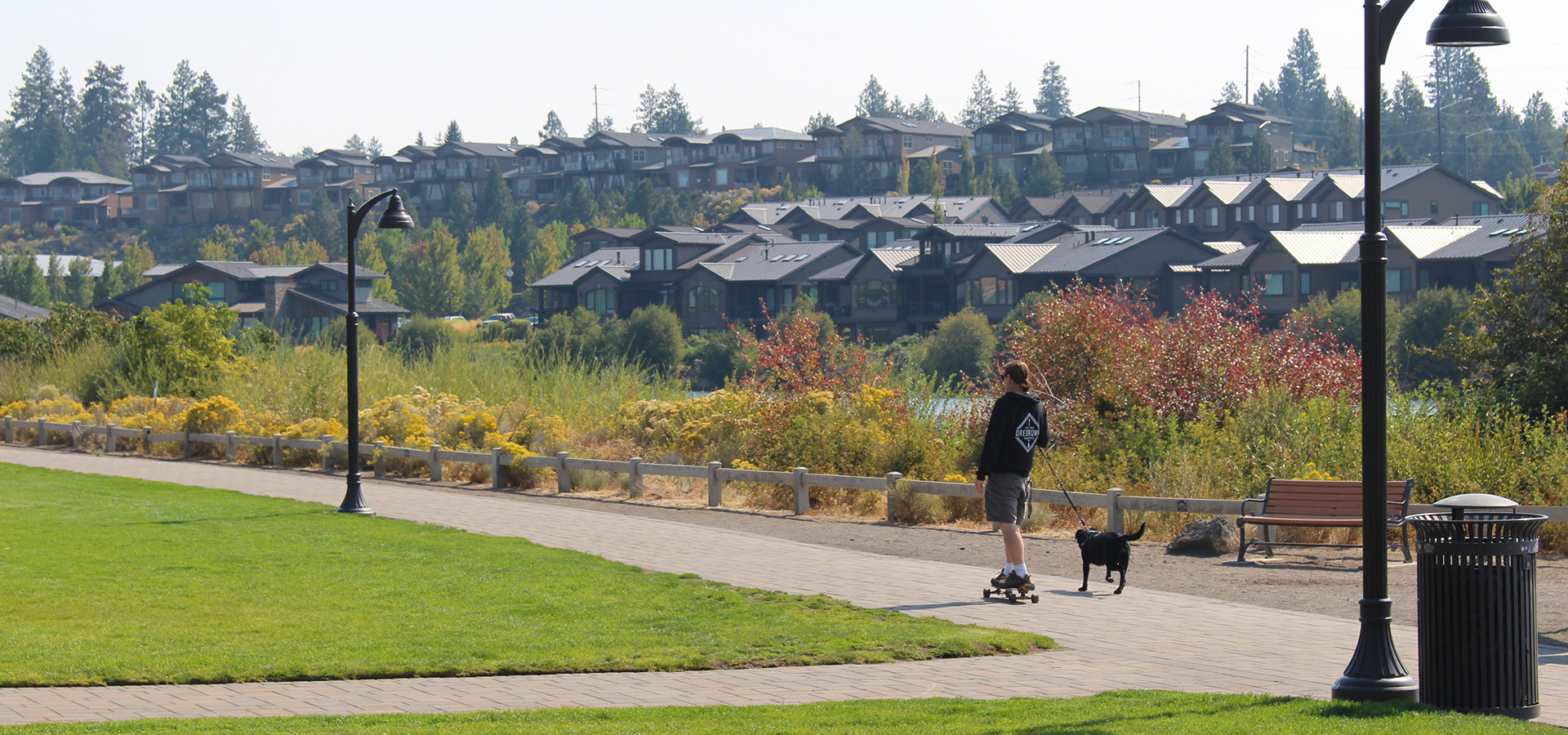 A man skateboarding with his dog at Riverbend Park.