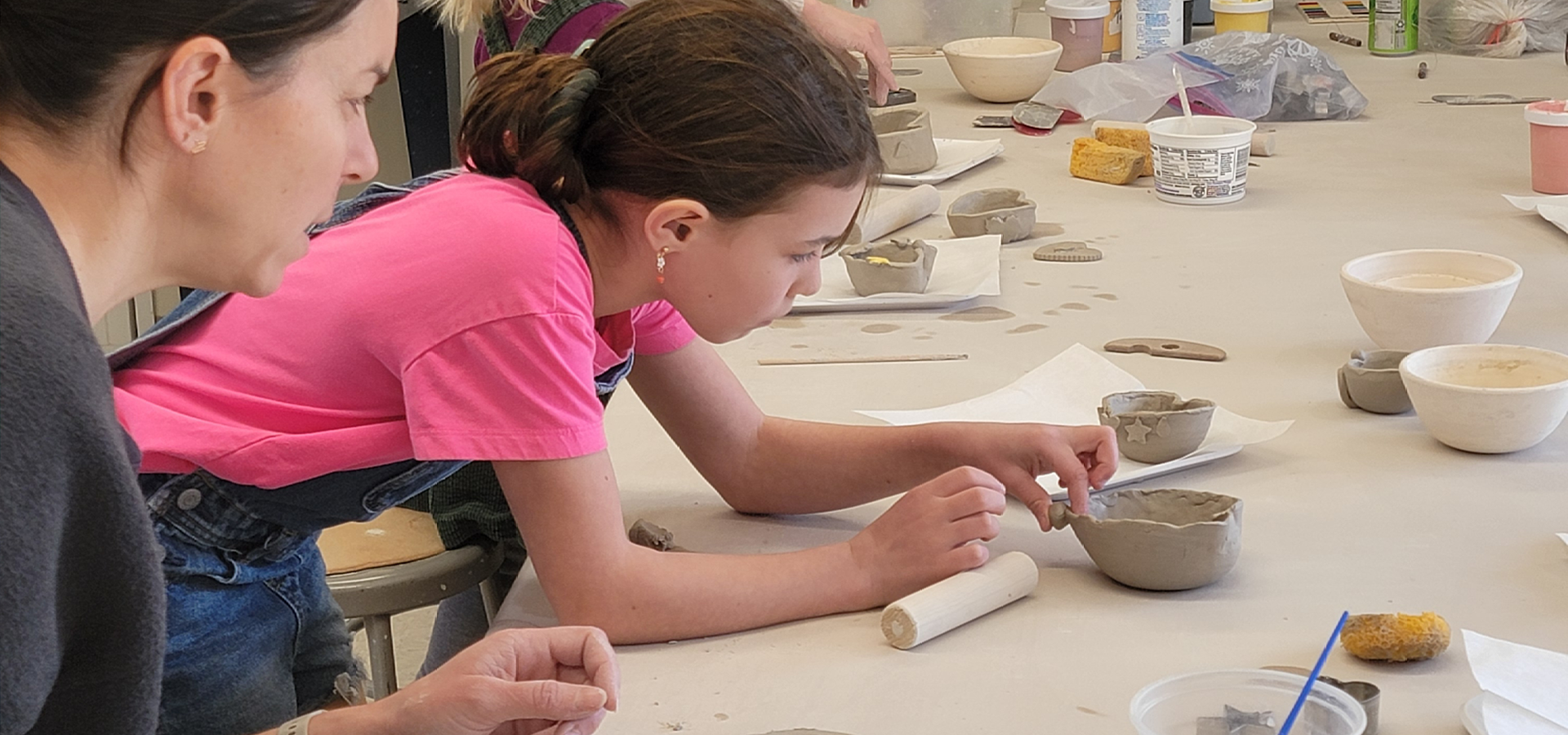 Close up of a child molding a handbuilt bowl while an adult overlooks