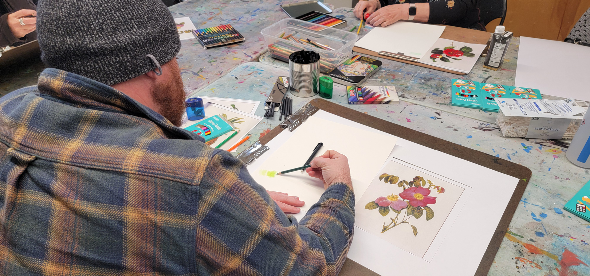 Over a shoulder, a man sketches a floral design with a colored pencil