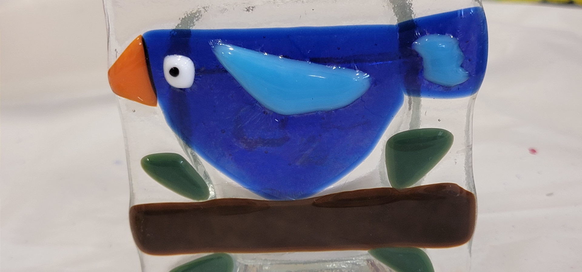 Close-up of simple fused glass design of a bird on a branch