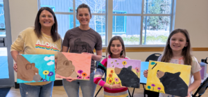 Two pairs of smiling adults and children with split dual paintings of bears smelling flowers