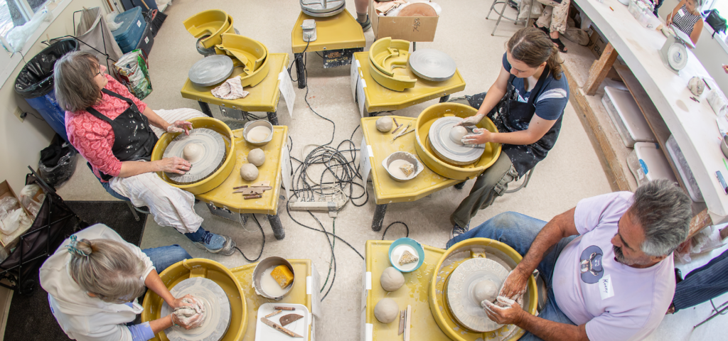 Overhead of a group of four adults working clay on the pottery wheels