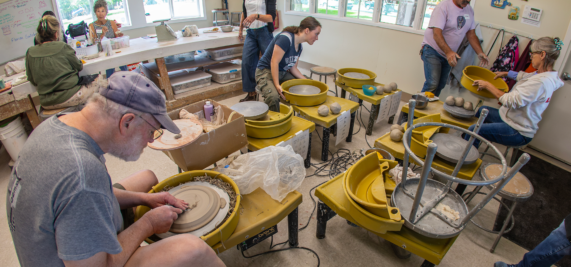 Seven adults work independently on pottery wheels and tables during pottery class