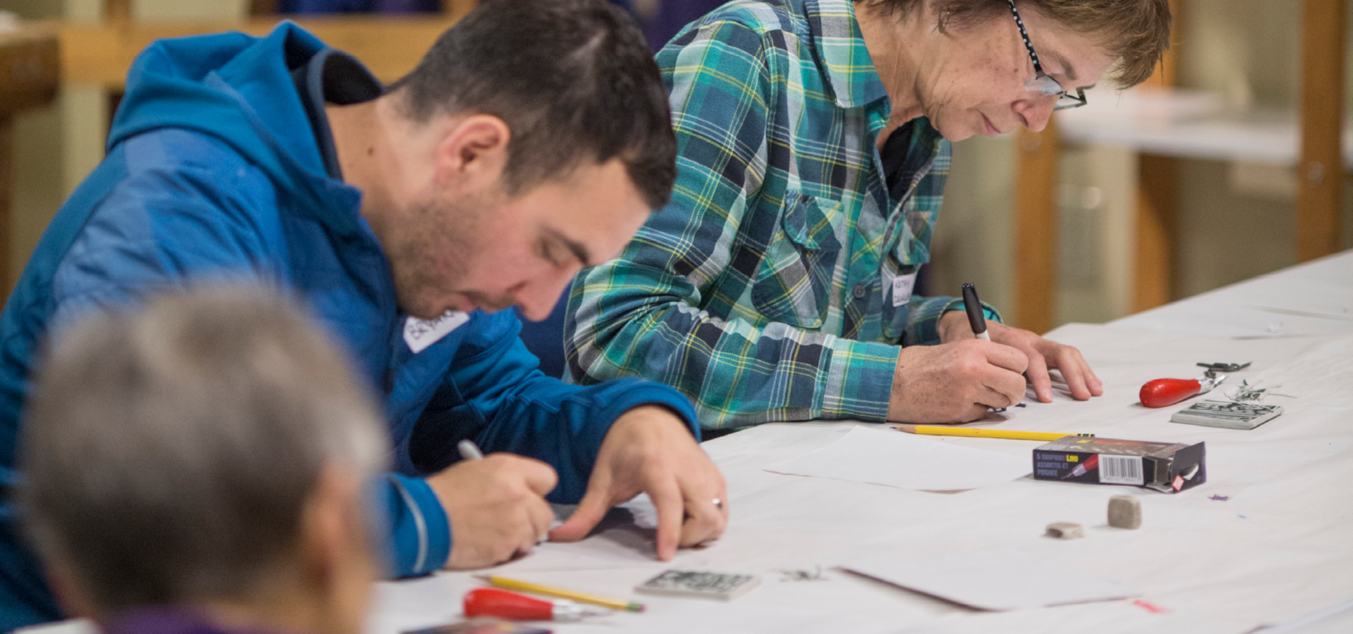 Two people work on a table while sketching out designs in a printmaking class