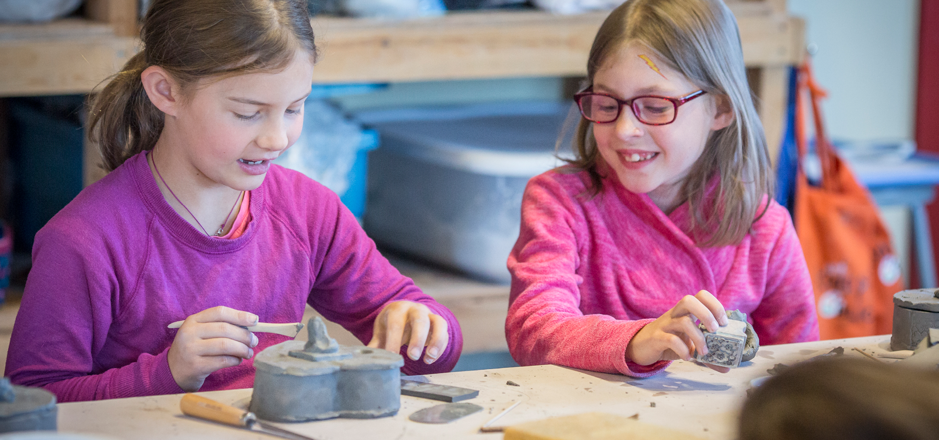 Two children engage with each other while working on handbuilt pottery in a class