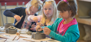 Three children work on handbuilt pottery pieces in a class