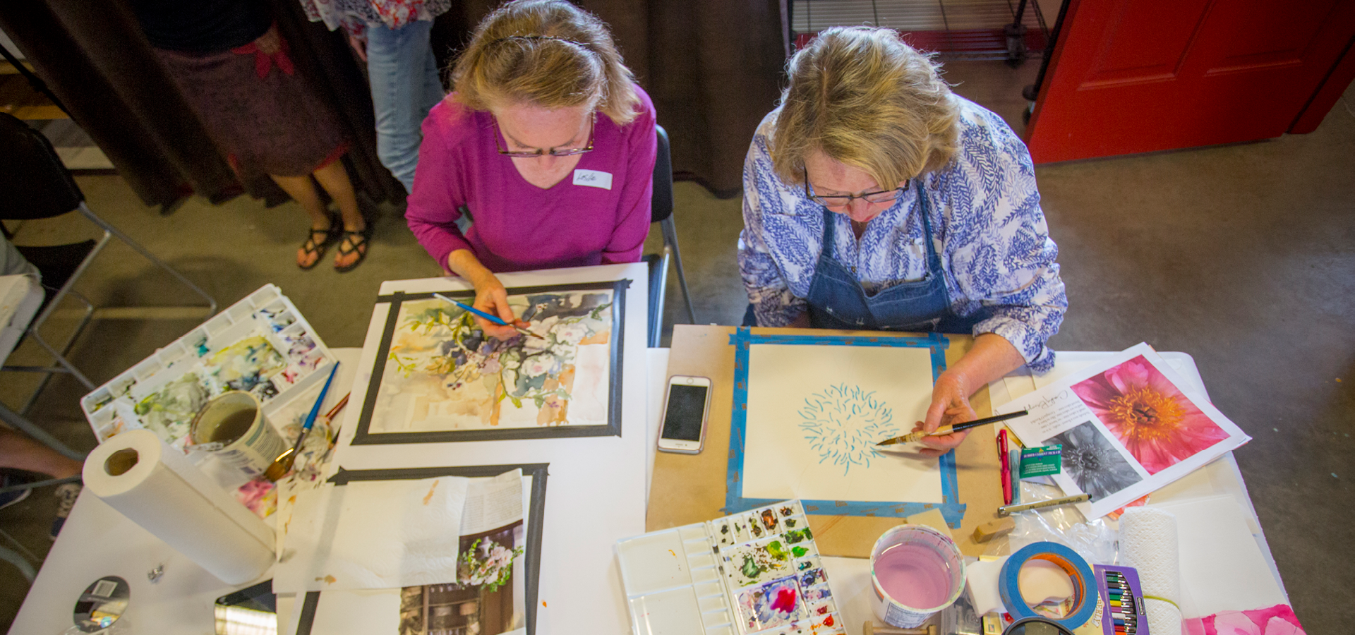 Two women paint floral artpieces in a watercolor class