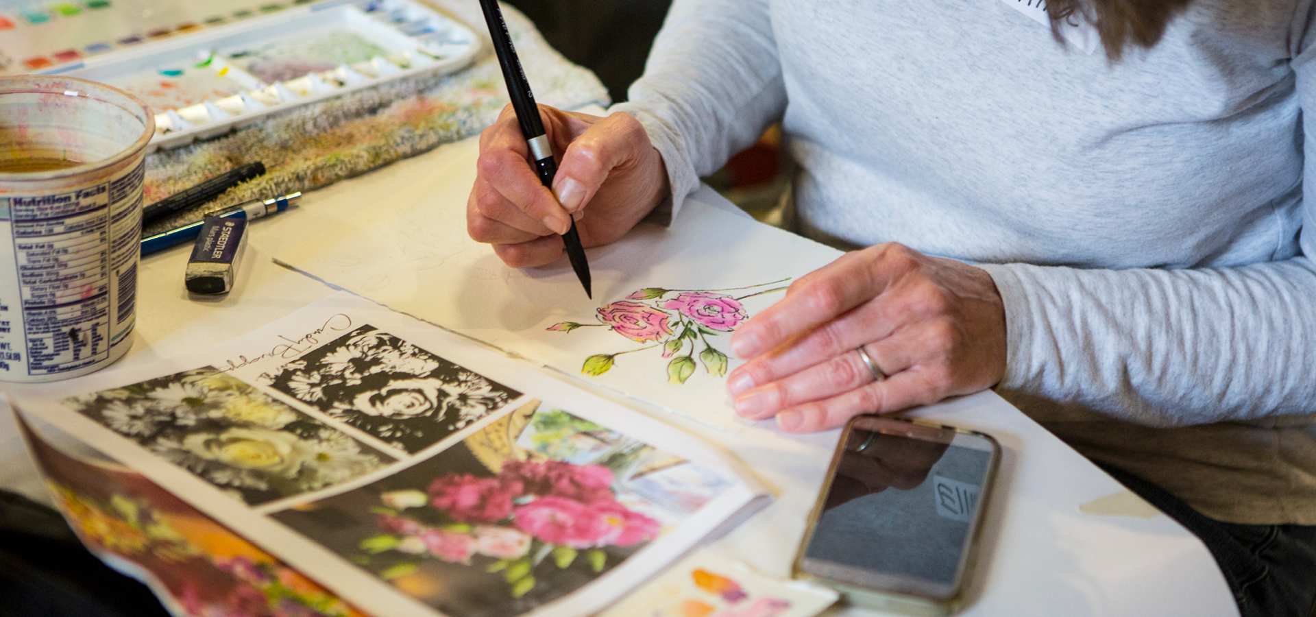 a close-up of hands with a fine brush, painting details on a painting of a rose