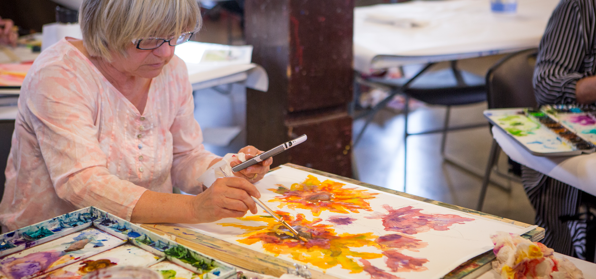 A woman paints large colorful floral artpiece in a watercolor class