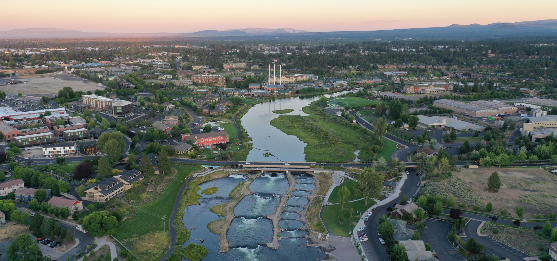 Aerial photograph of the sunset overlooking Bend Whitewater Park and the Old Mill District in the background.
