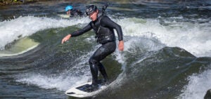 A man with a lifevest and helmet surfs the wave at White Water Park.