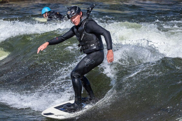 A man with a lifevest and helmet surfs the wave at White Water Park.