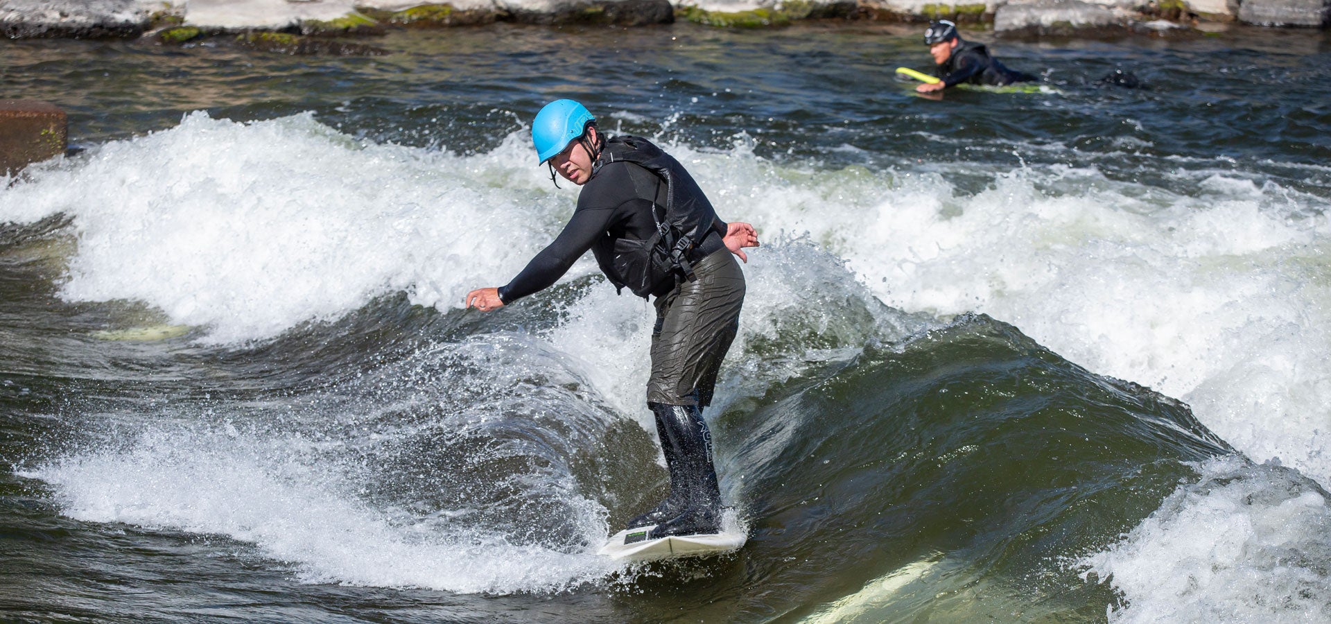 A surfer with helmet and life jacket rides the wave at Bend Whitewater Park