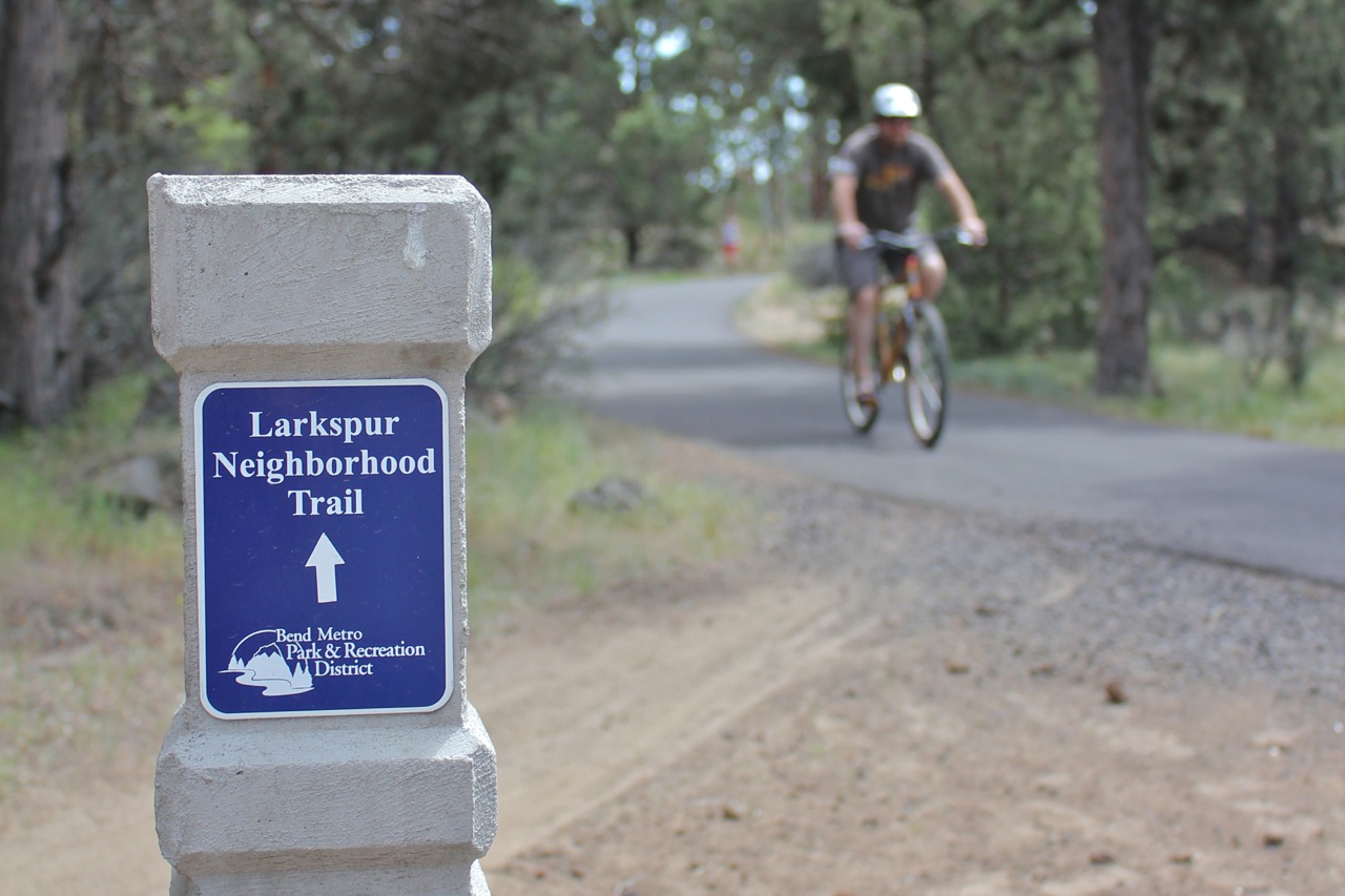 a larkspur trail sign with a man riding a bike in the background