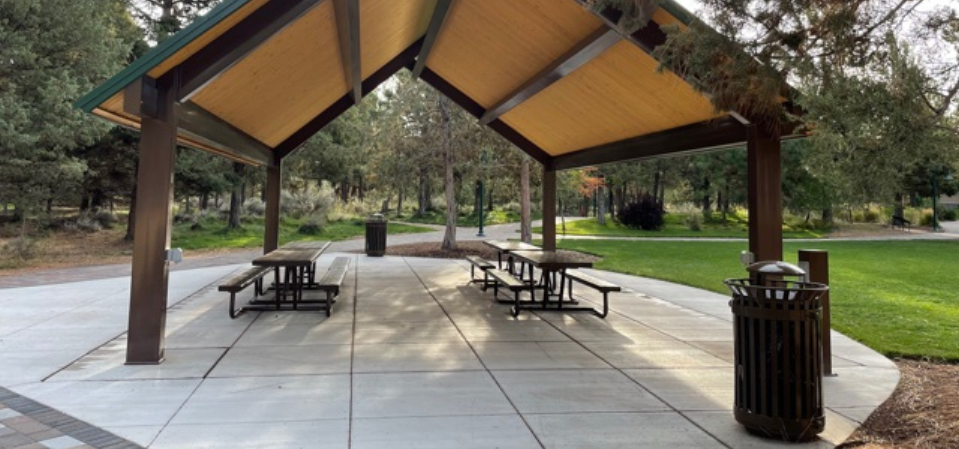 view of park benches under the picnic shelter at Larkspur park, trees and green lawn in the background