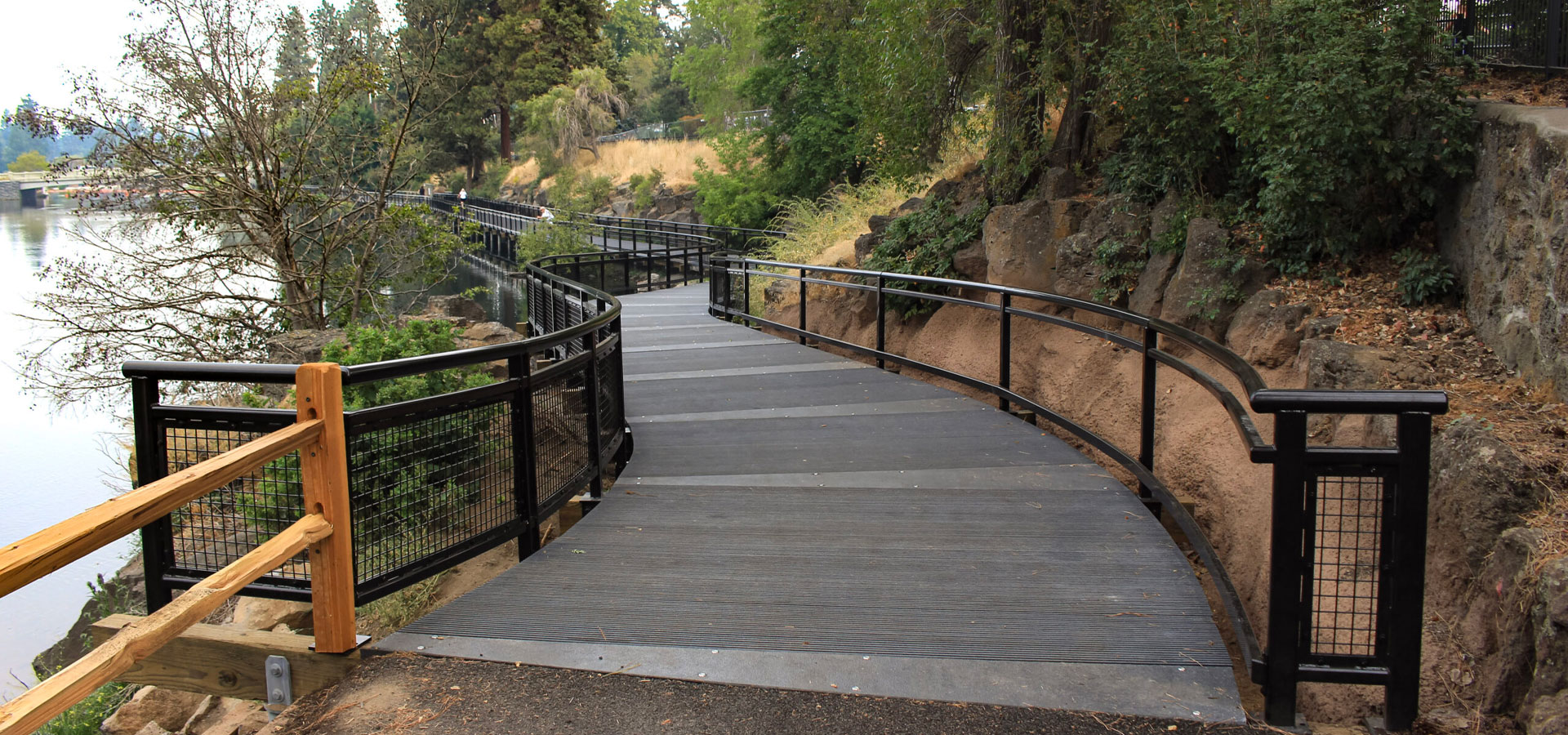 Southern entrance to the Drake Park boardwalk, flanked by the Deschutes river and the river bank with grass and trees