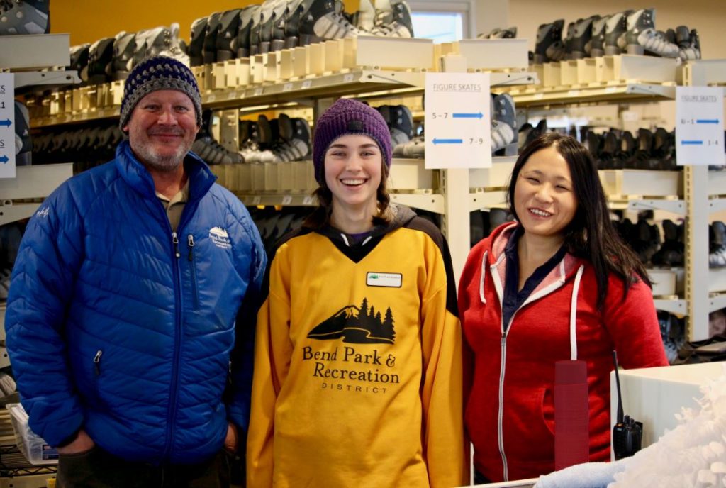 Three Pavilion employees smiling at the camera standing in front of skate racks.