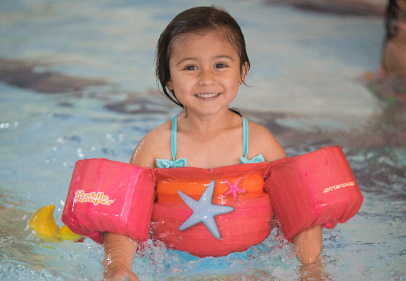 A young girl with water floaties on in a pool.