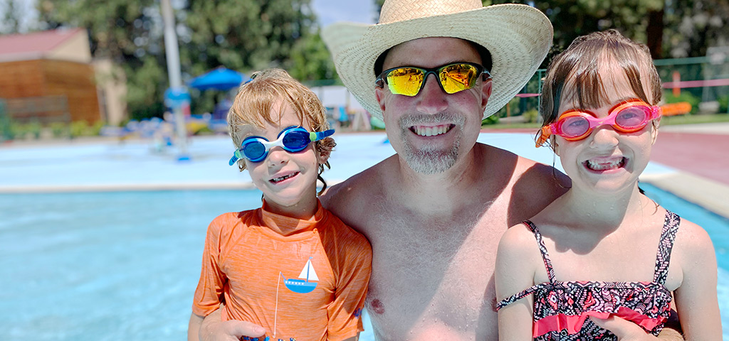 A man posing with two kids at the pool
