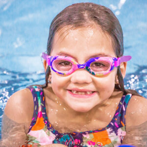 A little girl in goggles at the pool.