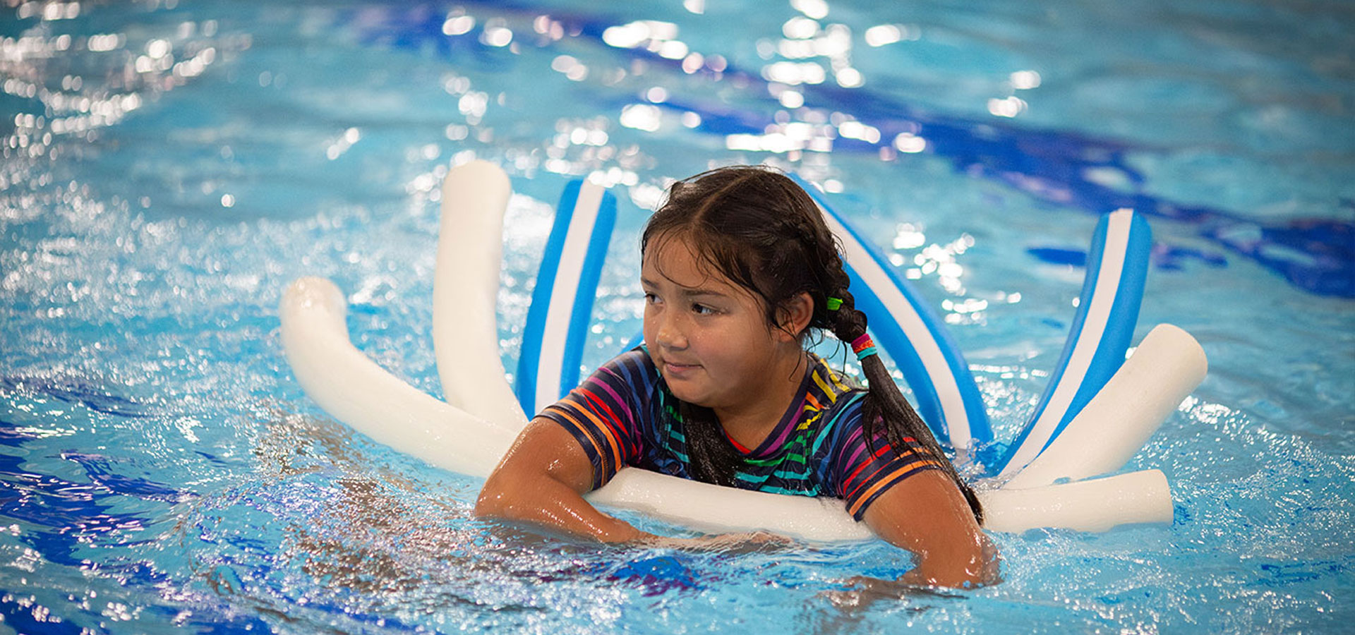 A young girl smiles while using floaties in the pool.