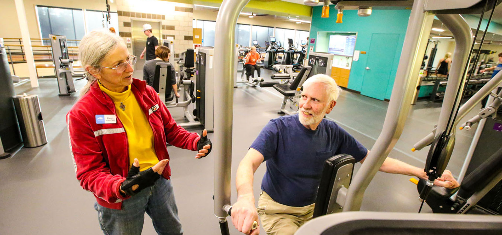 A volunteer assists a patron with using one of the fitness machines at Larkspur.