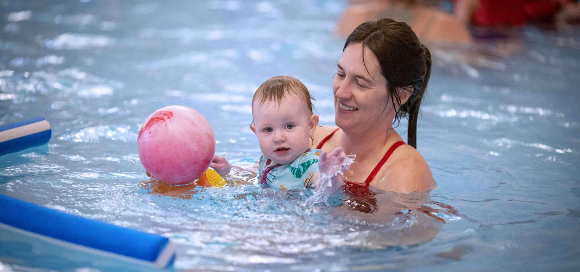 Mother playing with her young child in the pool at swim lessons.