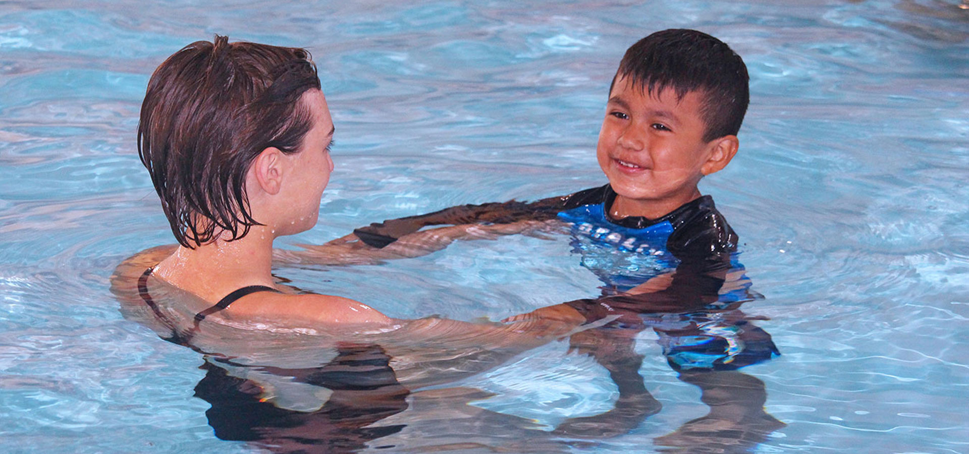 An instructor assists young boy during swim lessons.