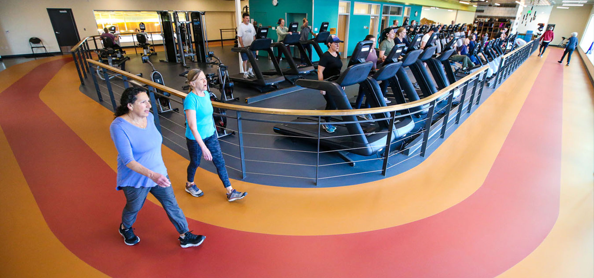 Two patrons walk around the indoor track at Larkspur while others use the running machines.