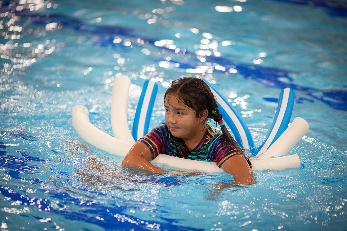 A young girl smiles while using floaties in the pool.