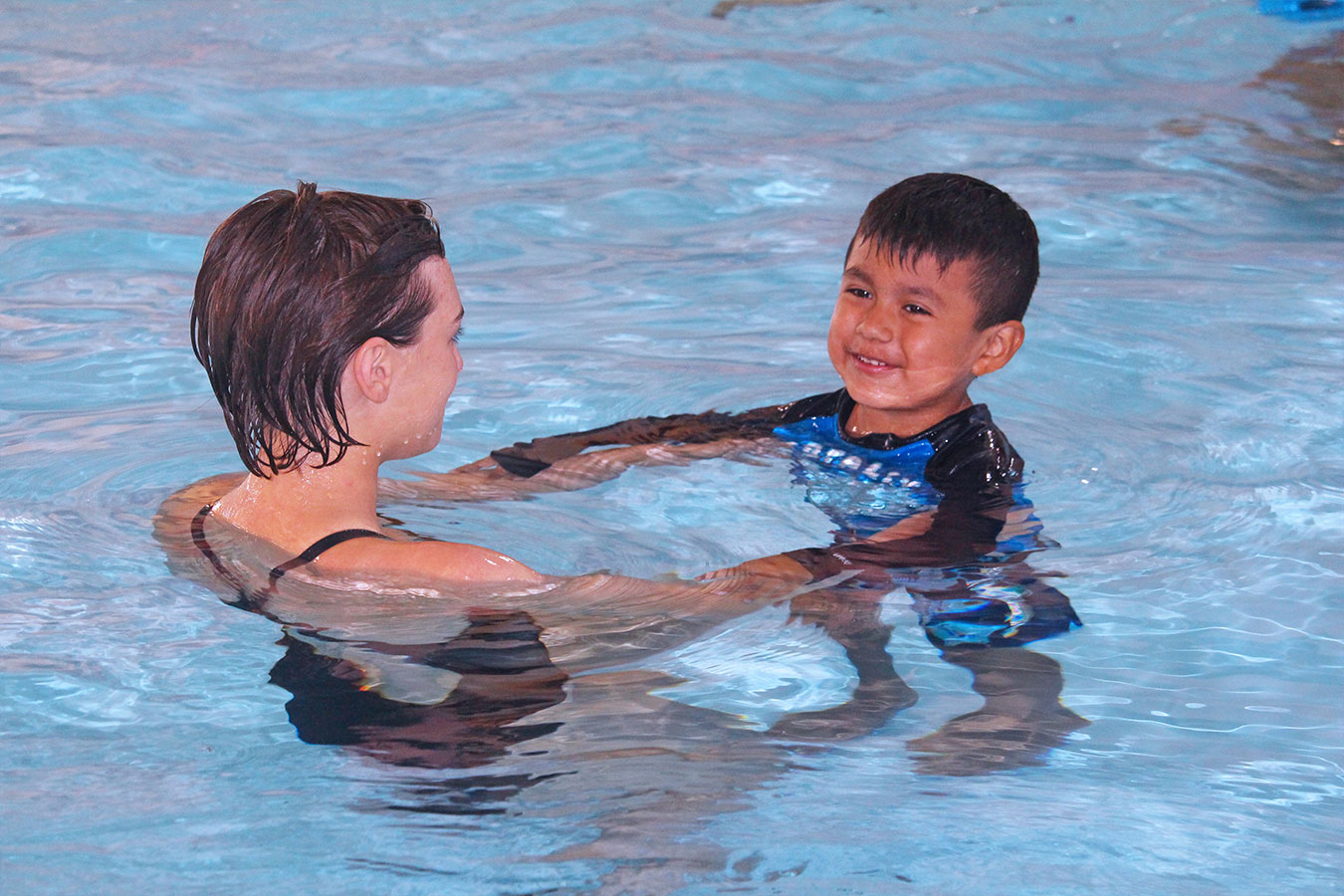An instructor assists young boy during swim lessons.