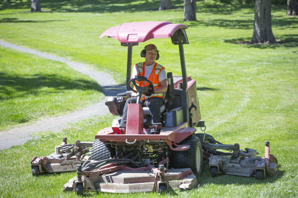 A BPRD maintenance worker in a riding lawnmower at a local park